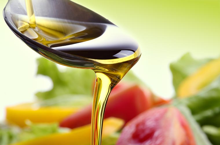Pflanzliches Öl tropft von einem Löffel – Symbol für Omega-3-Fettsäuren in gesunden Ölen wie Lein-, Raps- und Walnussöl.